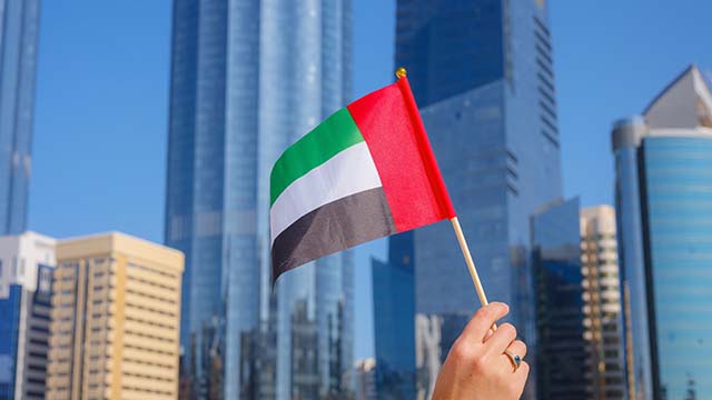 Hand holding a UAE flag in a modern city